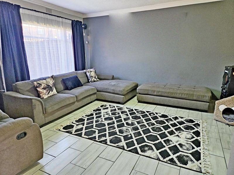 A well-maintained living room featuring light-colored tiled flooring, crown molding, and a large window allowing for natural light.