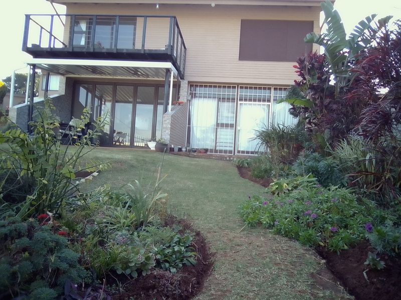 Rear view of the property featuring a landscaped garden, a raised balcony with metal railings, and sliding glass doors with security bars.