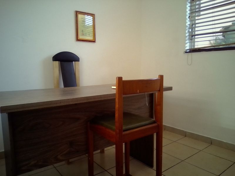 A functional office space featuring tiled flooring and window blinds, providing a simple and practical work environment.