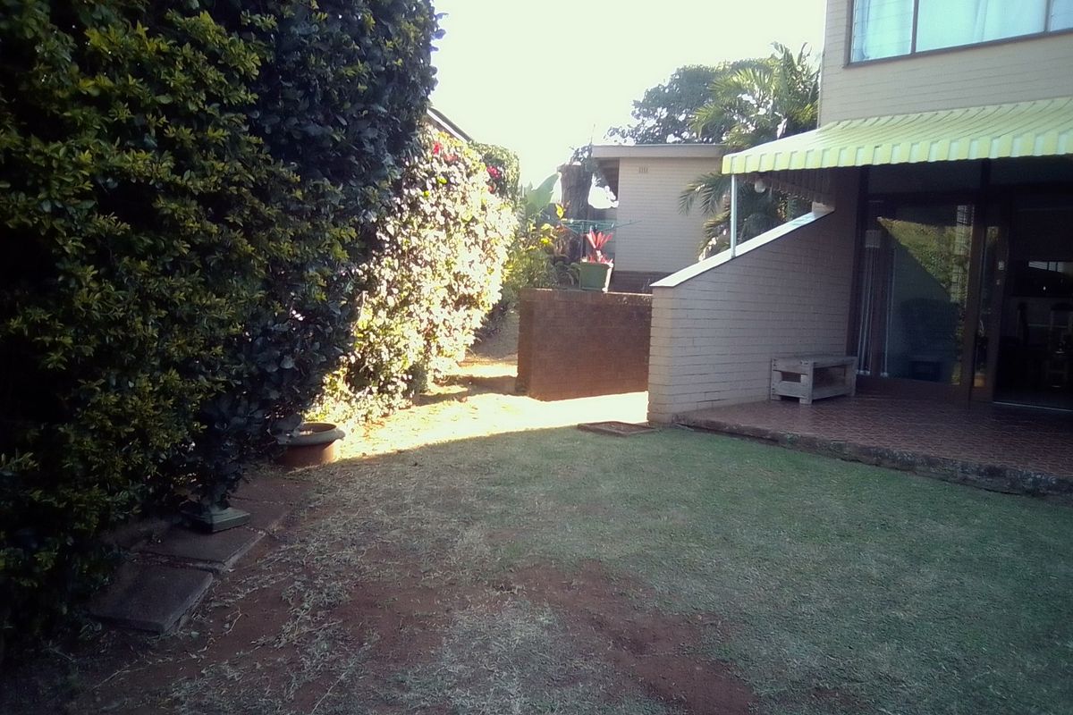 Rear garden area featuring a small tiled patio with a yellow striped awning and a lawn area bordered by established hedges.