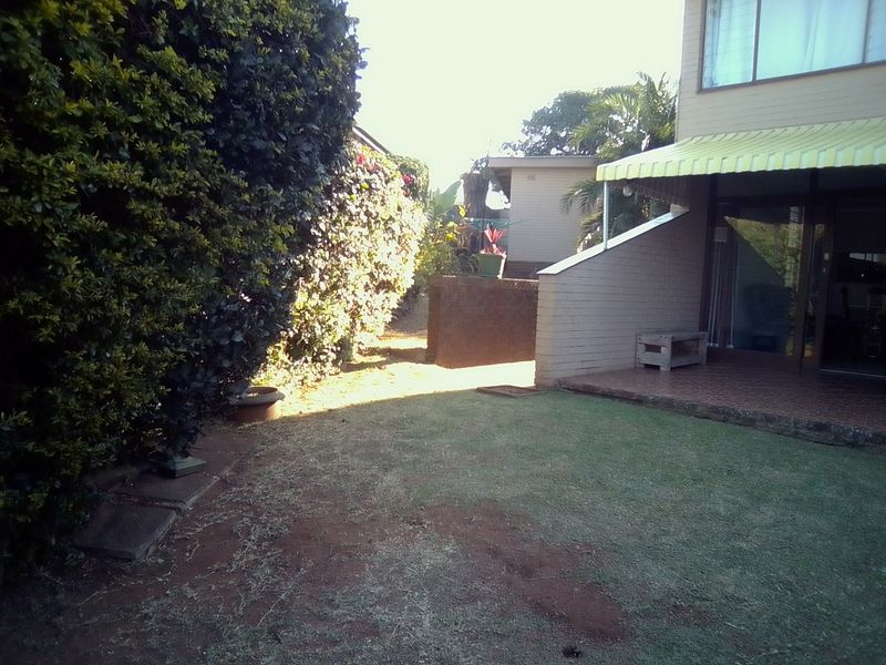Rear garden area featuring a small tiled patio with a yellow striped awning and a lawn area bordered by established hedges.