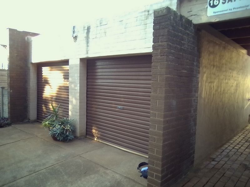 A double garage exterior featuring brown roller shutter doors, brick pillars, and a concrete driveway with visible signs of weathering.