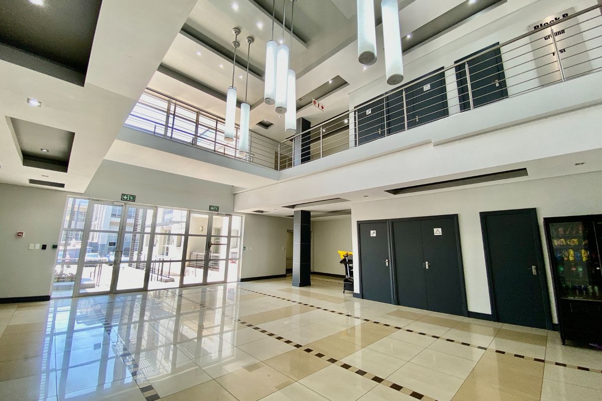 Spacious double-volume commercial entrance lobby featuring modern tiled flooring, stainless steel balustrades, and contemporary pendant lighting with a mezzanine level.