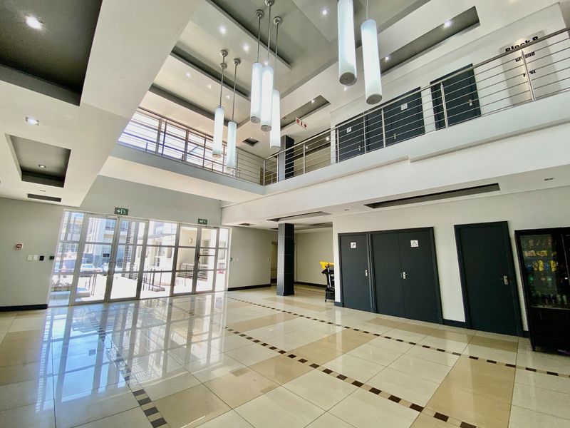 Spacious double-volume commercial entrance lobby featuring modern tiled flooring, stainless steel balustrades, and contemporary pendant lighting with a mezzanine level.