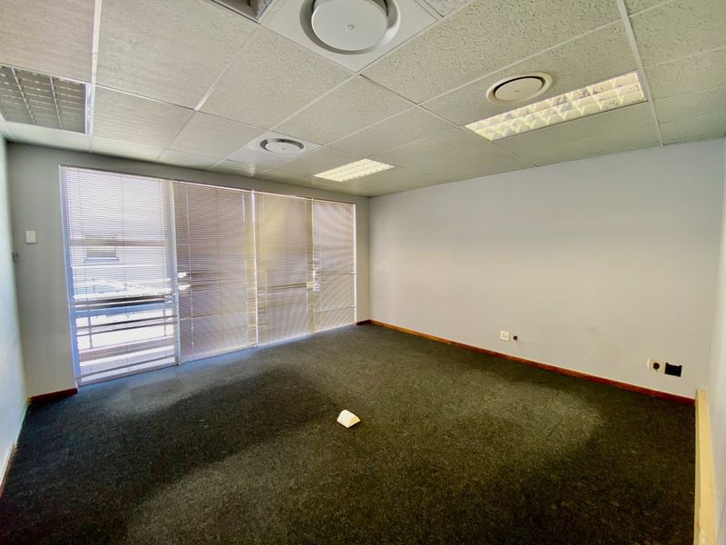 A vacant commercial office space featuring a suspended ceiling, recessed lighting, air conditioning vents, and large windows with venetian blinds.