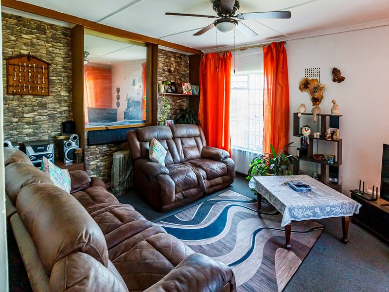 A living room featuring a stone accent wall, ceiling fan, and large window with security bars, offering a dated aesthetic ready for modernization.