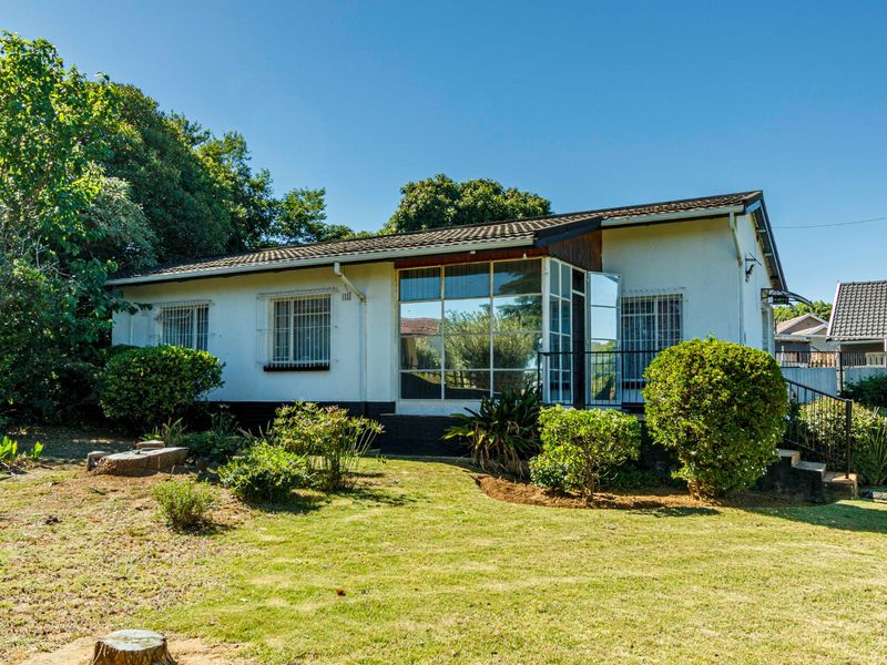 Rear view of a single-story house featuring a large glass-enclosed sunroom, security window bars, and a spacious garden area.