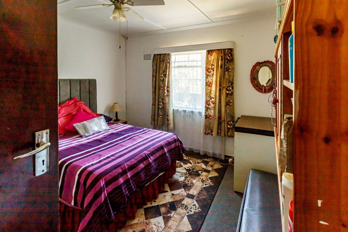 A functional bedroom featuring a ceiling fan and a window with security bars, providing a comfortable and secure living space.
