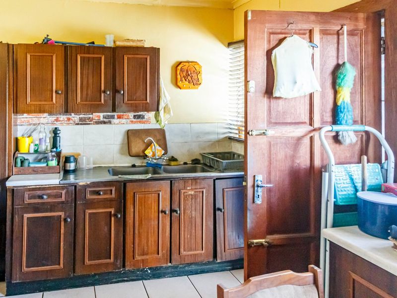 A dated kitchen featuring traditional wooden cabinetry, a stainless steel sink, and tiled backsplash, requiring cosmetic updates to modernize the space.