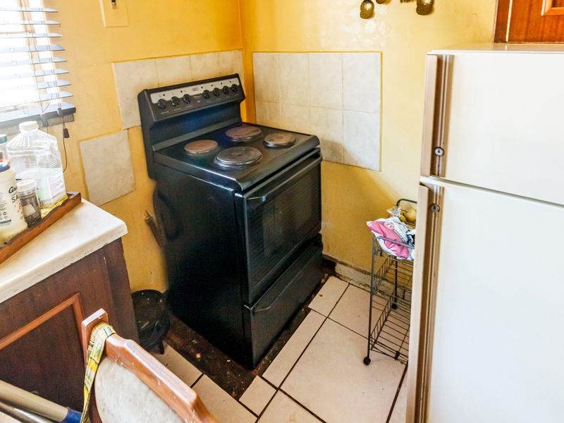 A compact kitchen area featuring a freestanding stove, tiled splashback, and tiled flooring, requiring cosmetic updates to improve the overall finish.