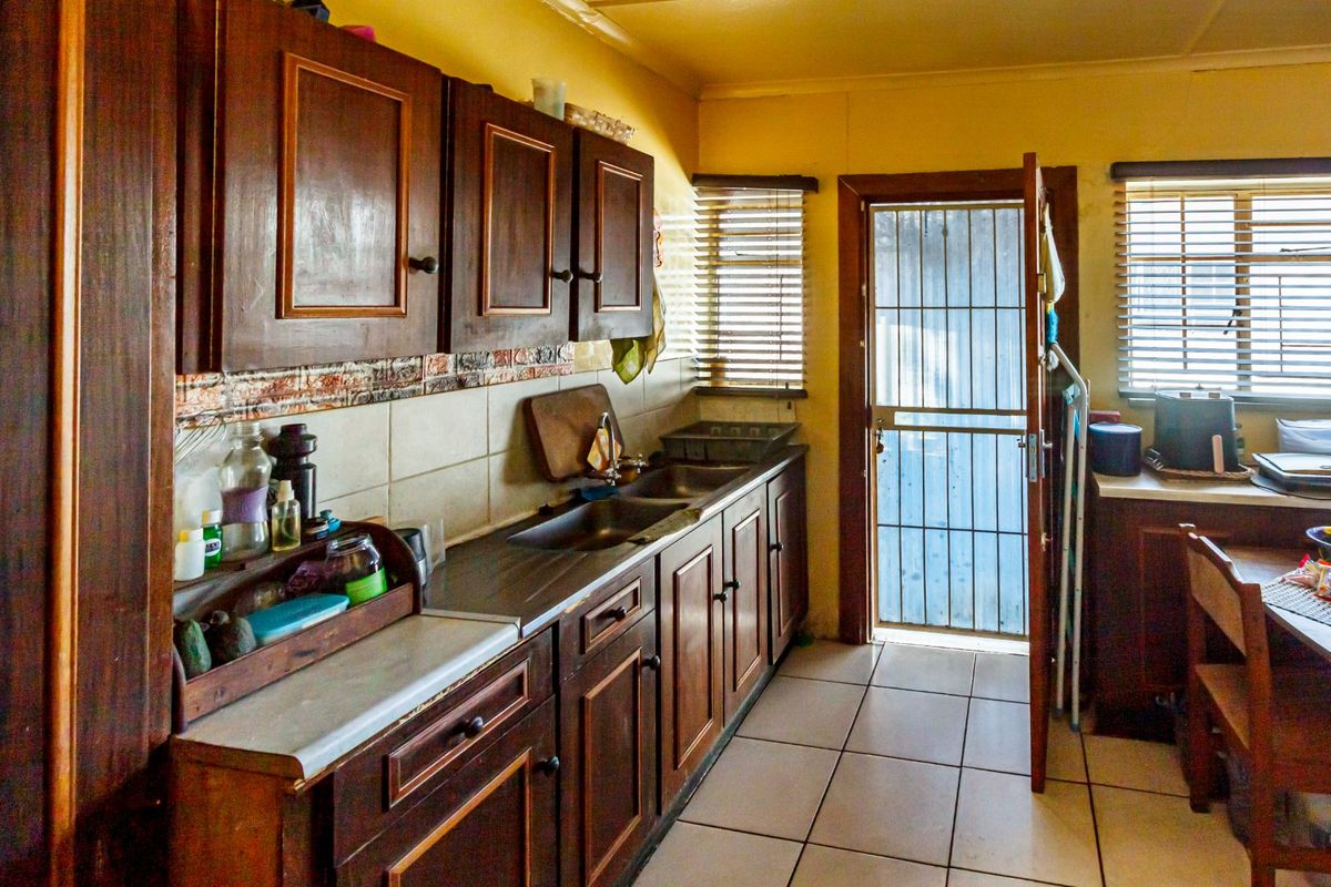 A functional kitchen featuring dark wooden cabinetry, a double stainless steel sink, tiled backsplash, and direct access to the exterior via a security gate.