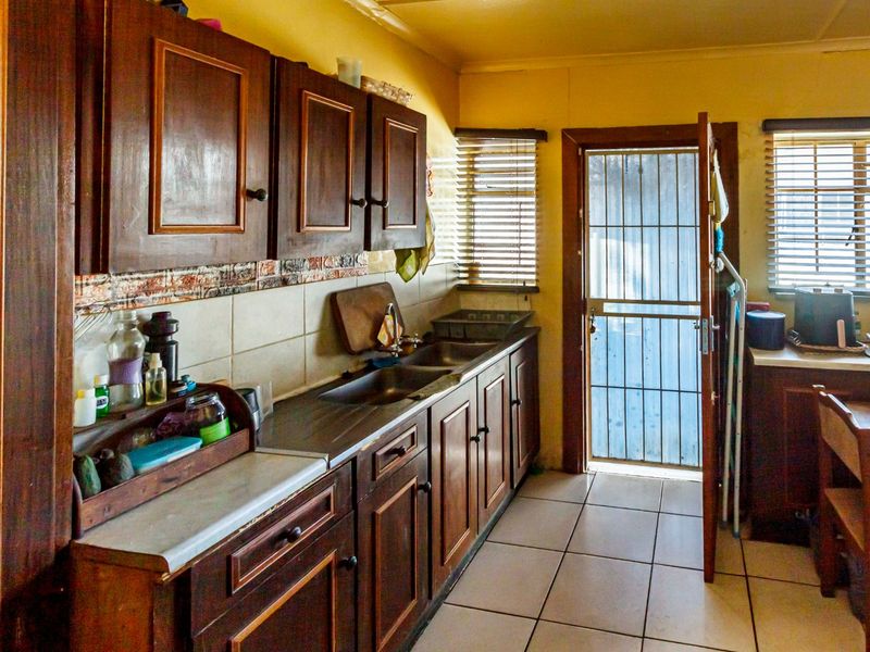 A functional kitchen featuring dark wooden cabinetry, a double stainless steel sink, tiled backsplash, and direct access to the exterior via a security gate.