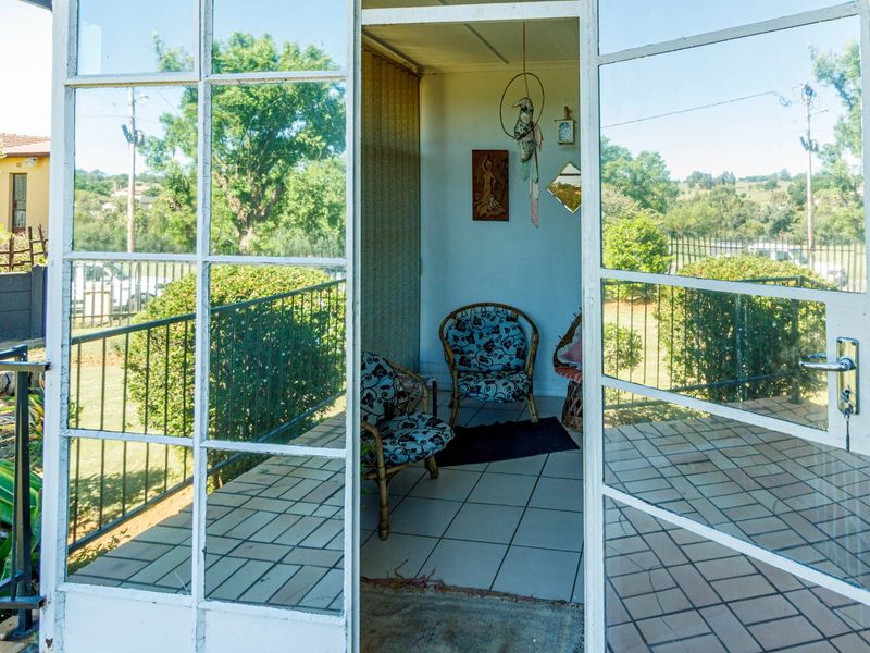 A covered patio area featuring tiled flooring and large metal-framed glass doors, offering a view of the surrounding garden and landscape.
