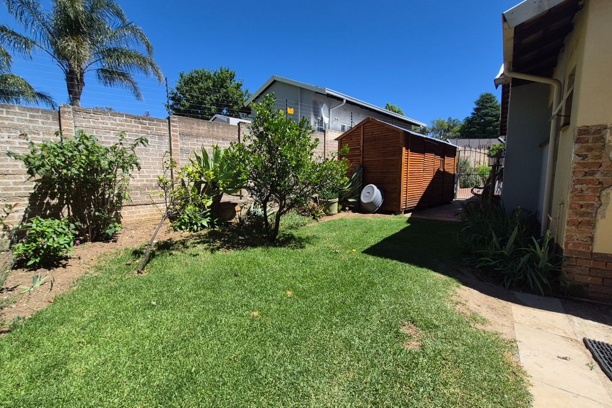 A rear garden area featuring a lawn, established trees, a wooden storage shed, and a brick boundary wall with electric fencing.