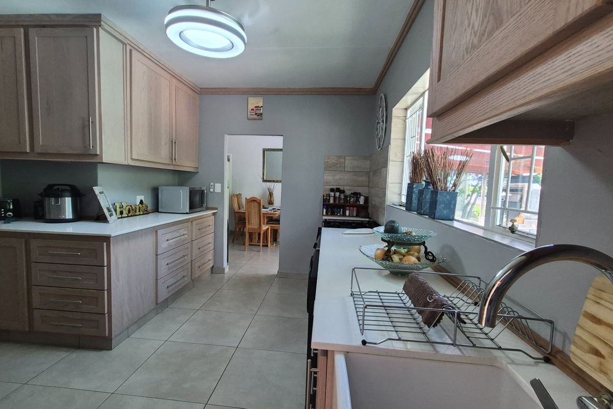 A functional kitchen featuring light wood cabinetry, stone countertops, an undermount sink, and tiled flooring, with a clear view into the adjacent dining area.