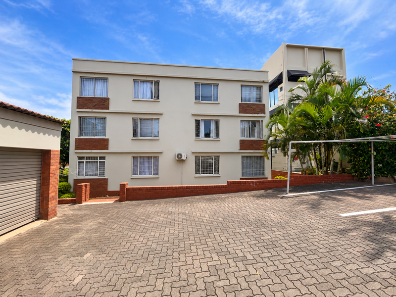 Exterior view of a multi-story apartment building featuring brick paving, a garage, and established landscaping.