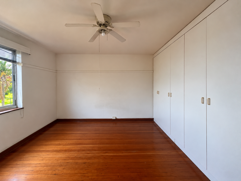 A spacious, empty bedroom featuring polished timber flooring, built-in cupboards, and a ceiling fan, offering a clean canvas for personalization.