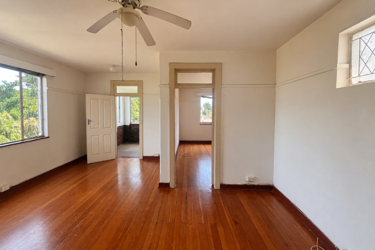 Spacious, empty living area featuring polished hardwood floors, a ceiling fan, and classic timber door frames, offering a bright and versatile living space.