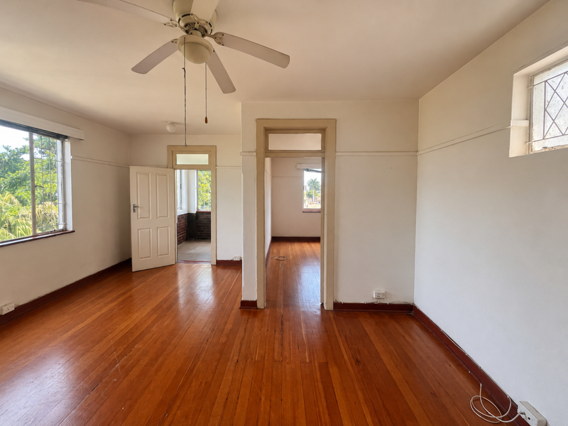 Spacious, empty living area featuring polished hardwood floors, a ceiling fan, and classic timber door frames, offering a bright and versatile living space.