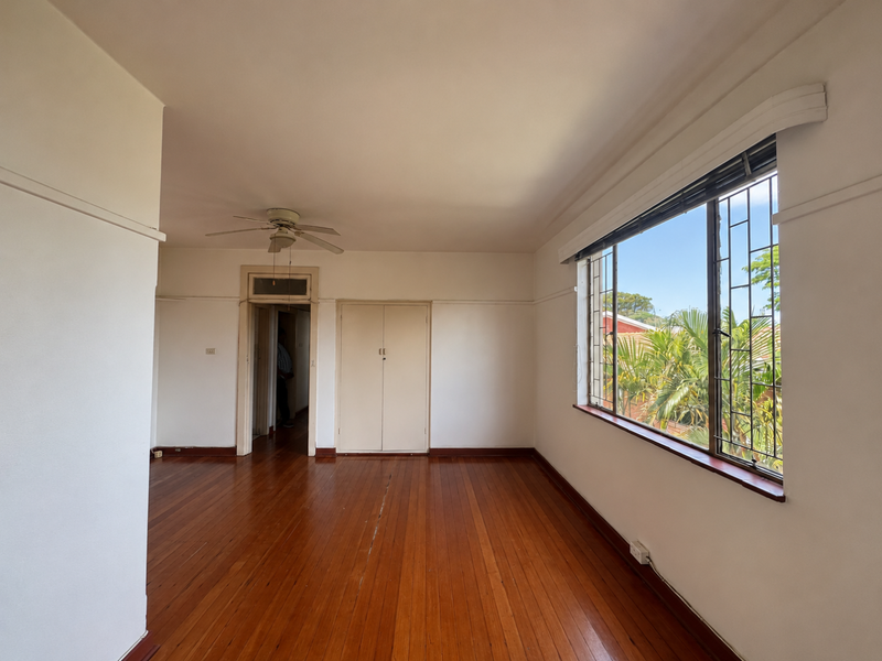 Spacious bedroom featuring original hardwood flooring, a ceiling fan, and built-in storage, offering a bright and airy atmosphere with large windows.