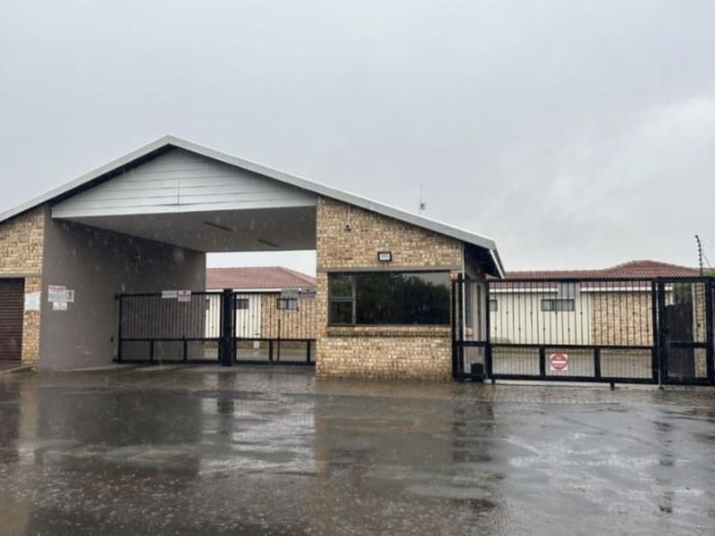 Front entrance view of a secure residential complex featuring a guard house, automated security gates, and paved driveway access.