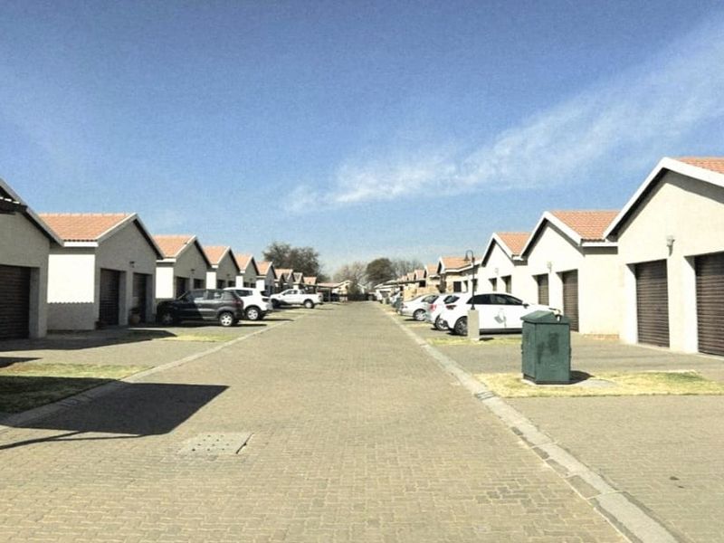 A view of a residential complex street featuring rows of houses with paved driveways and garage access.