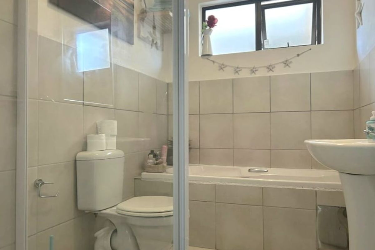 A functional bathroom featuring a built-in bathtub, pedestal sink, toilet, and tiled finishes, providing a practical space for daily use.