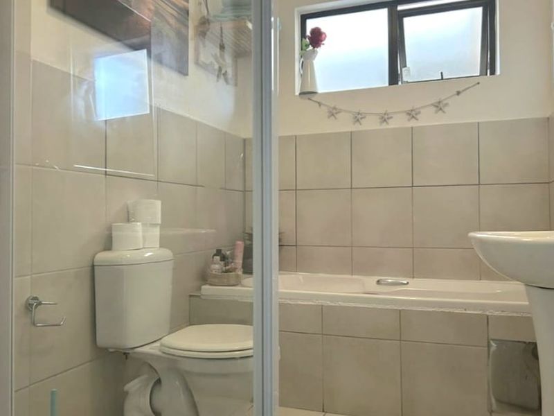 A functional bathroom featuring a built-in bathtub, pedestal sink, toilet, and tiled finishes, providing a practical space for daily use.