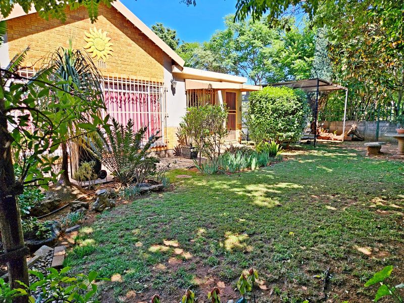 A view of the rear garden featuring a well-maintained lawn, established landscaping, and a covered patio area attached to the brick house.