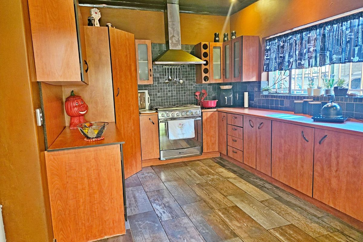 A functional kitchen featuring wooden cabinetry, a stainless steel oven with extractor fan, tiled backsplash, and wood-look flooring.