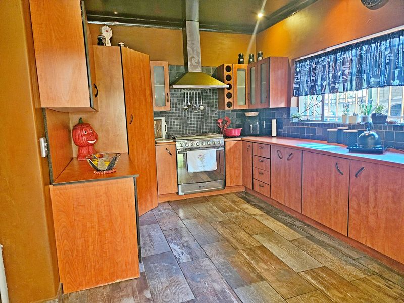 A functional kitchen featuring wooden cabinetry, a stainless steel oven with extractor fan, tiled backsplash, and wood-look flooring.