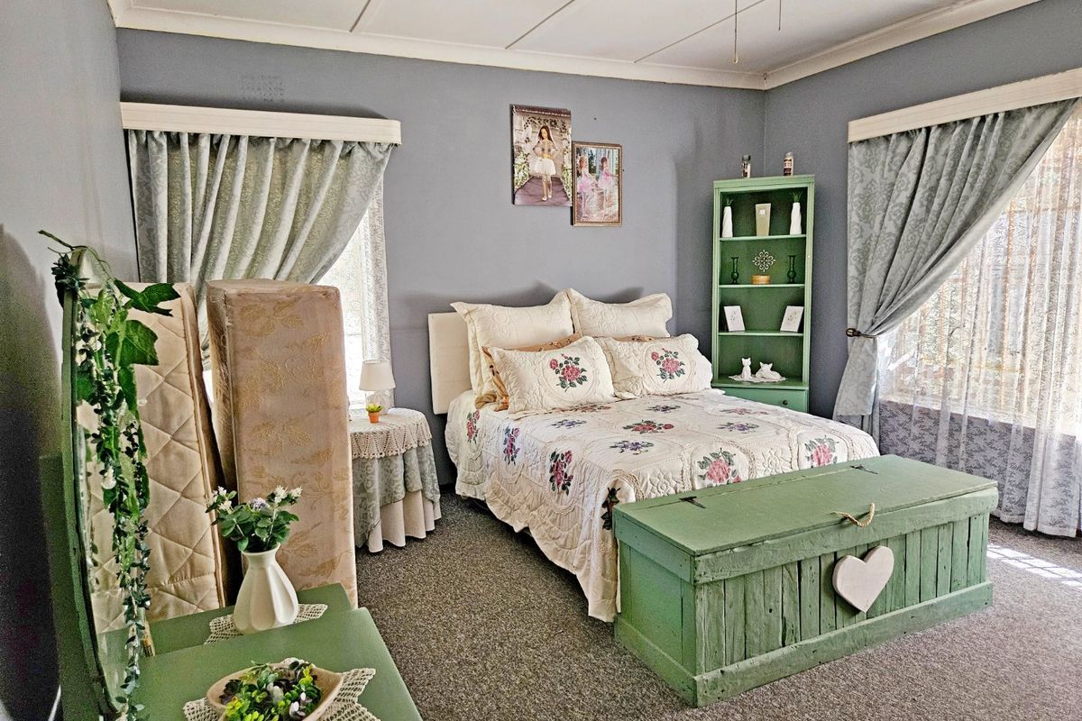 A bedroom featuring grey walls, carpeted flooring, and a ceiling fan, with dual windows dressed in curtains.