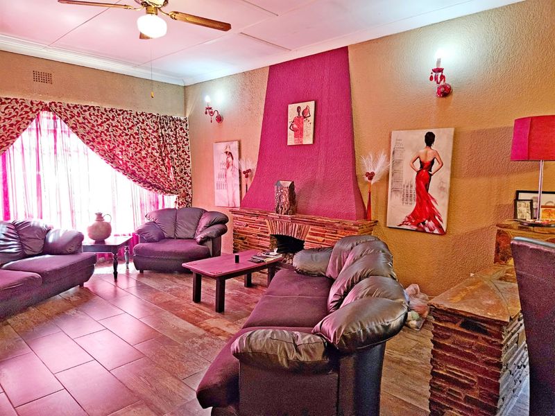 Living room featuring a prominent stone fireplace, tiled flooring, and ceiling fan, with dated wall finishes and lighting fixtures.