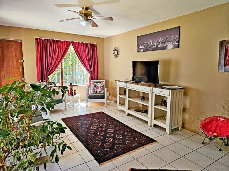 A living room featuring tiled flooring, a ceiling fan, and security bars on the window, with neutral wall tones.