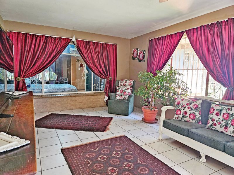 A living room featuring tiled flooring and large windows with security bars, offering a functional space with potential for modern updates.