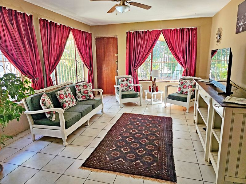 A living room featuring tiled flooring, a ceiling fan, and large windows fitted with security bars.