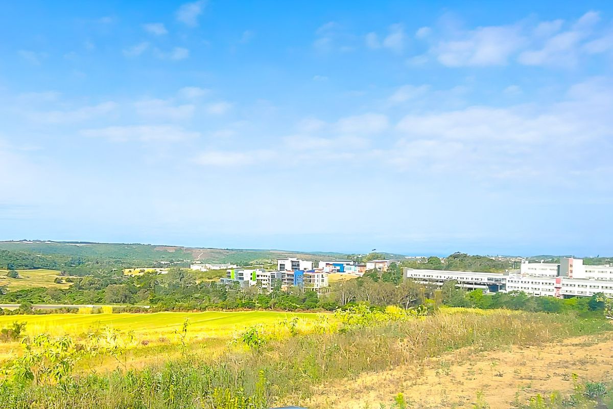 A scenic landscape view overlooking open fields and distant commercial buildings under a clear blue sky.
