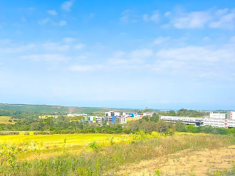 A scenic landscape view overlooking open fields and distant commercial buildings under a clear blue sky.