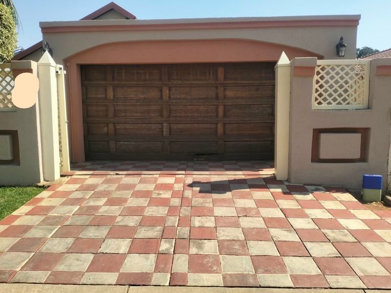 A single garage featuring a wooden door and a distinctive checkered paved driveway, set within a masonry boundary wall with decorative lattice detailing.
