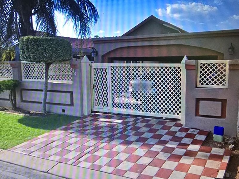 Front exterior view of the property featuring a paved driveway, secure lattice gate, and a well-maintained boundary wall.