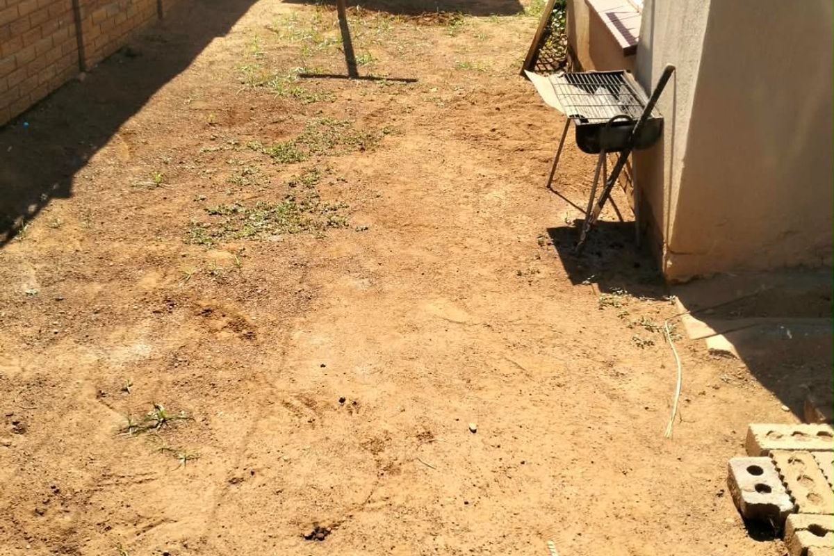 A rear garden area featuring a brick boundary wall, a wooden storage shed, and an unlandscaped dirt yard.