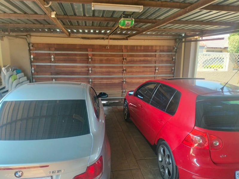 A functional double garage featuring a wooden sectional door, tiled flooring, and an exposed steel roof structure with an automated door motor.