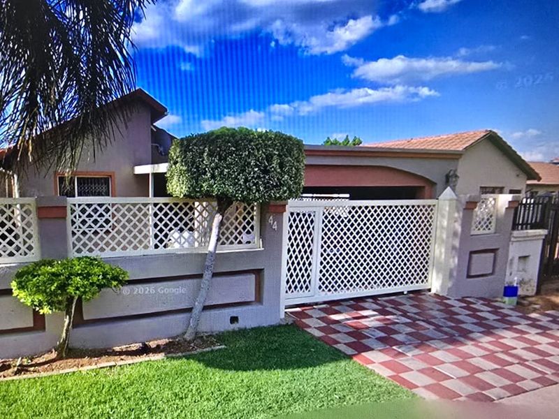 Front elevation of the property featuring a secure perimeter wall with lattice fencing, a sliding gate, and a paved driveway.