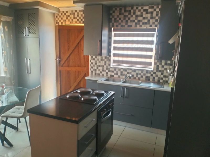 Modern kitchen featuring dark grey cabinetry, a central island with a built-in oven and hob, tiled splashback, and tiled flooring.