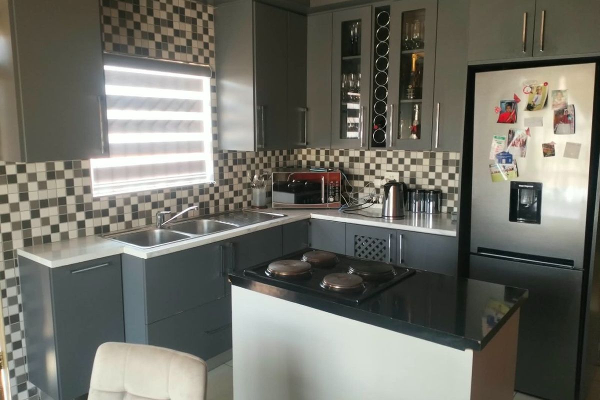 A modern kitchen featuring dark grey cabinetry, contrasting stone countertops, a tiled mosaic backsplash, and a central island with a built-in hob.