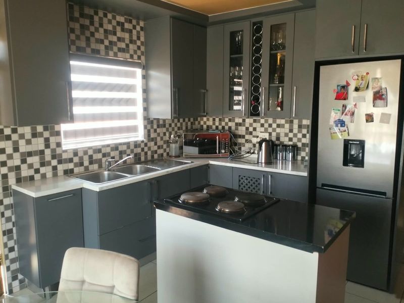 A modern kitchen featuring dark grey cabinetry, contrasting stone countertops, a tiled mosaic backsplash, and a central island with a built-in hob.