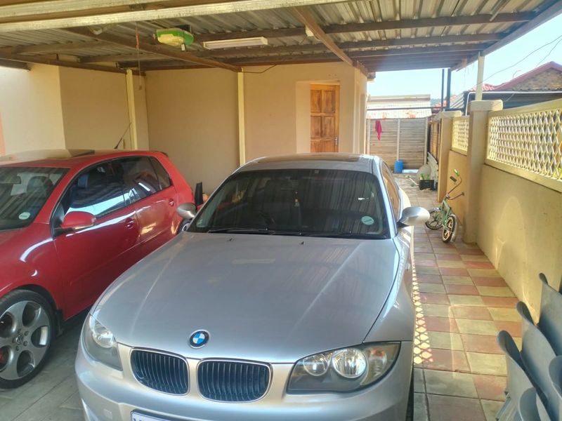 A covered carport or garage area featuring tiled flooring and a corrugated metal roof structure.