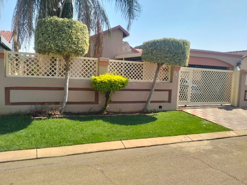 Front elevation of the property featuring a secure boundary wall with lattice detailing, a sliding gate, and a paved driveway.