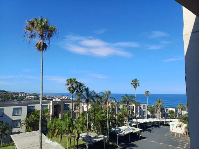 Elevated view overlooking the apartment complex grounds, featuring covered parking bays and a scenic ocean backdrop.