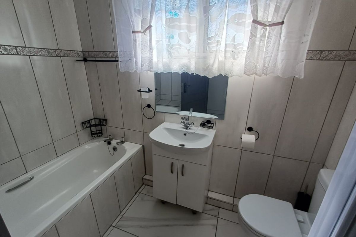 A functional bathroom featuring a bathtub, vanity cabinet with washbasin, and toilet, finished with neutral wall and floor tiling.
